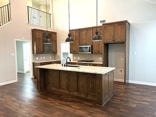 kitchen with pendant lighting, a high ceiling, a center island with sink, sink, and light stone counters