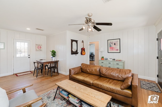 living room with light wood-type flooring, baseboards, visible vents, and crown molding