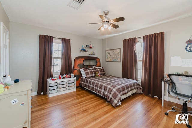 bedroom with light wood-style floors, ceiling fan, visible vents, and baseboards