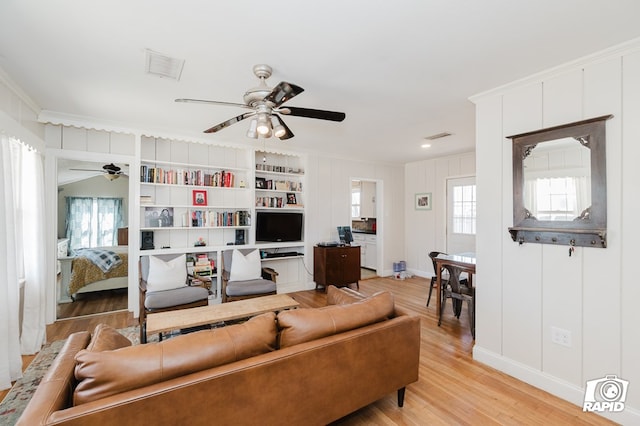 living area with crown molding, a ceiling fan, visible vents, and light wood-style floors