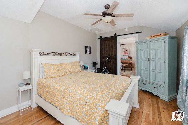 bedroom featuring lofted ceiling, a barn door, a ceiling fan, light wood-type flooring, and baseboards