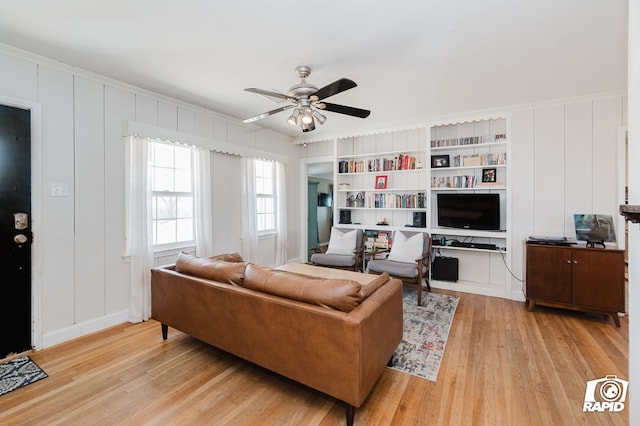 living area featuring light wood-type flooring, ceiling fan, built in shelves, and a decorative wall