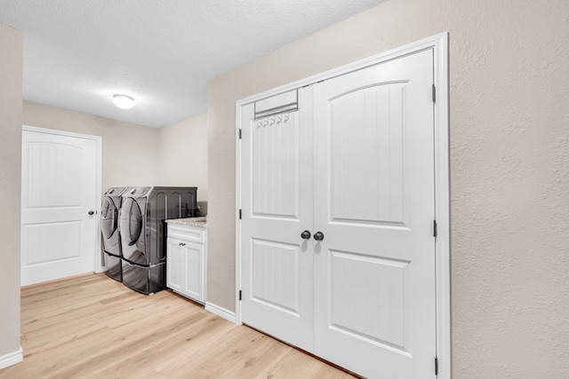 10606 E County Rd 104, Midland, TX 79706 - laundry room with washing machine and clothes dryer, light wood-style floors, cabinet space, a textured wall, and a textured ceiling