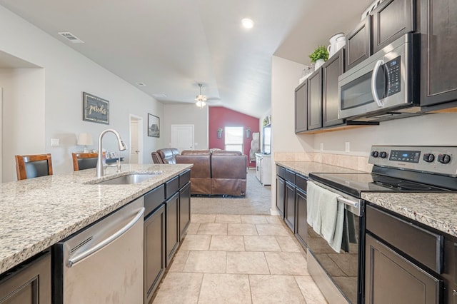 kitchen featuring appliances with stainless steel finishes, lofted ceiling, sink, light stone countertops, and dark brown cabinets