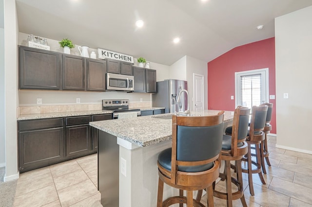 kitchen with appliances with stainless steel finishes, sink, a kitchen breakfast bar, dark brown cabinetry, and a center island with sink