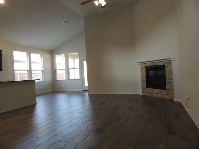 unfurnished living room with high vaulted ceiling, dark hardwood / wood-style floors, a stone fireplace, and ceiling fan