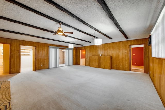 unfurnished room featuring a wealth of natural light, a textured ceiling, wood walls, ceiling fan, and beam ceiling