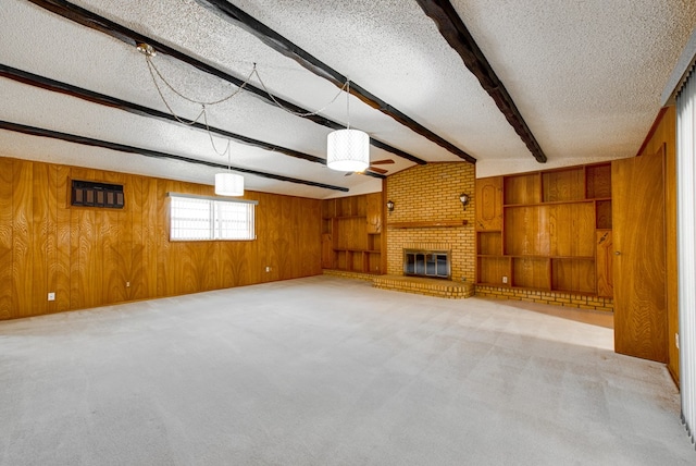 unfurnished living room featuring light carpet, wood walls, a brick fireplace, a textured ceiling, and beamed ceiling