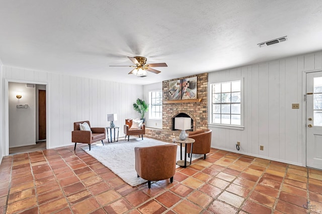 living room with ceiling fan, wooden walls, and a brick fireplace