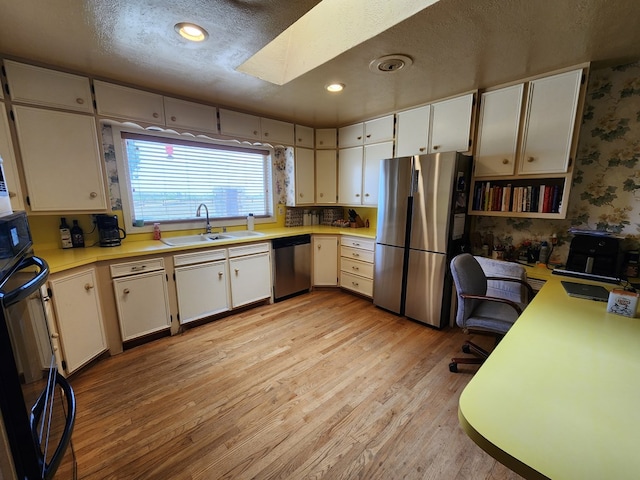 kitchen with white cabinets, sink, light wood-type flooring, a textured ceiling, and appliances with stainless steel finishes