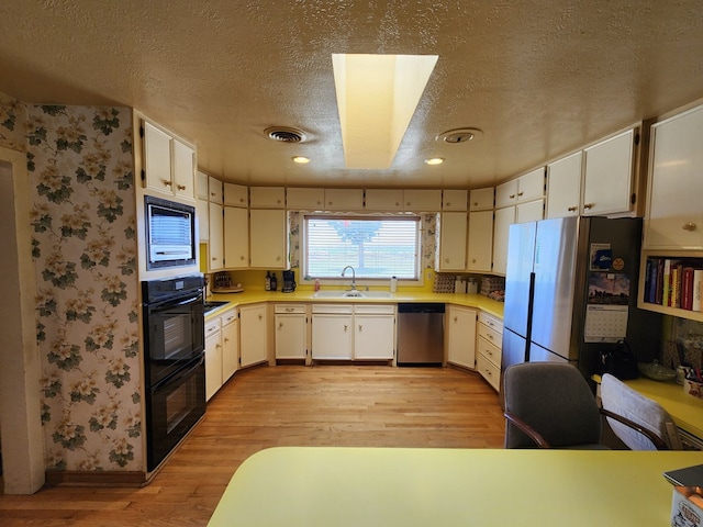 kitchen with sink, a textured ceiling, appliances with stainless steel finishes, light hardwood / wood-style floors, and white cabinetry