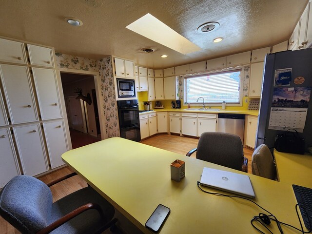 kitchen with a skylight, sink, a textured ceiling, white cabinets, and black appliances