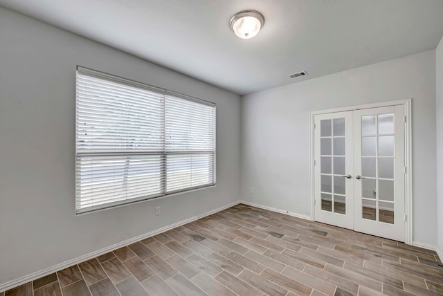 unfurnished room with wood finished floors, visible vents, baseboards, and french doors