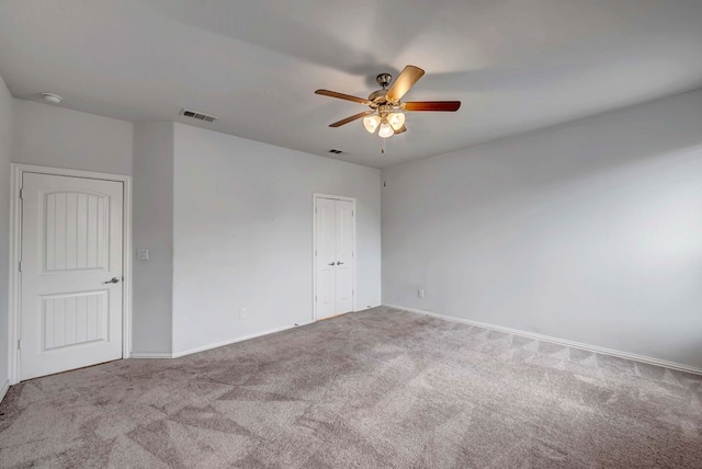 carpeted spare room with visible vents, baseboards, and ceiling fan