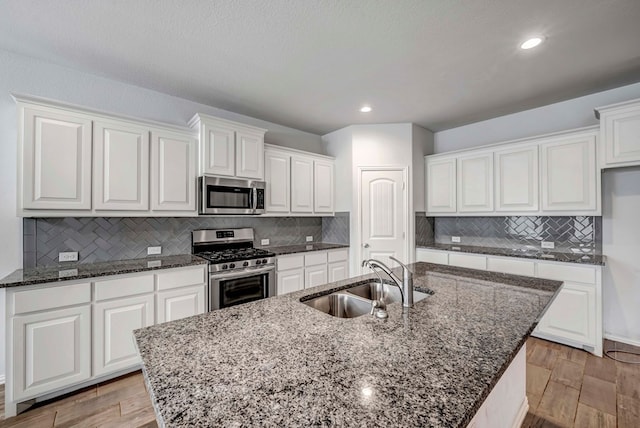 kitchen featuring white cabinets, stainless steel appliances, a kitchen island with sink, a sink, and decorative backsplash