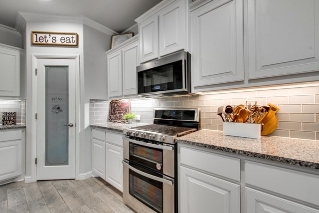 kitchen with light stone counters, ornamental molding, white cabinets, appliances with stainless steel finishes, and backsplash