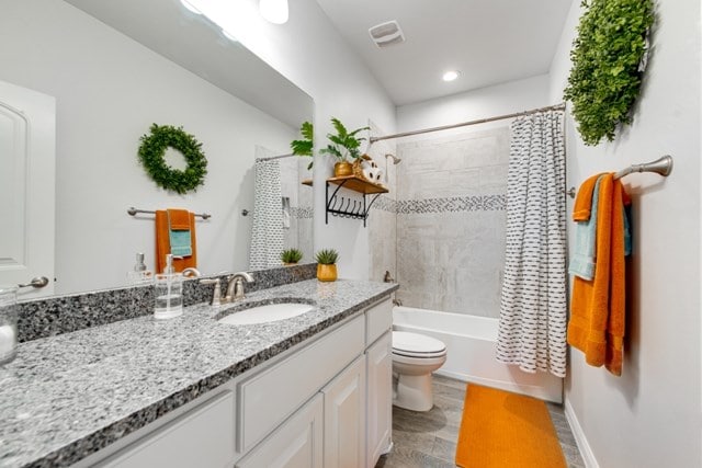 bathroom featuring vanity, wood finished floors, visible vents, shower / bath combo with shower curtain, and toilet