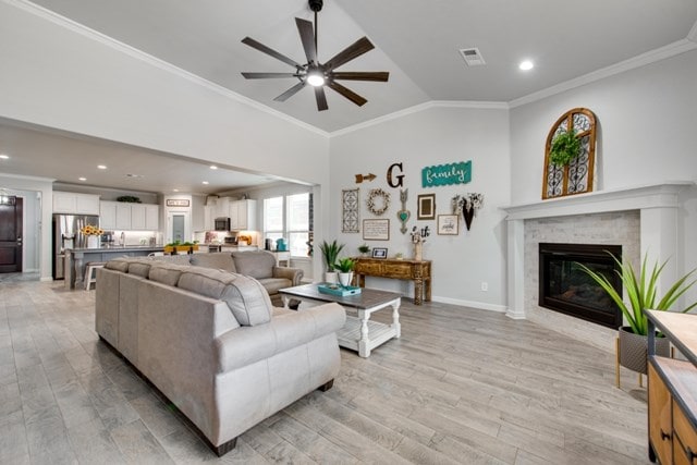 living area with visible vents, ornamental molding, light wood-style floors, a fireplace, and vaulted ceiling