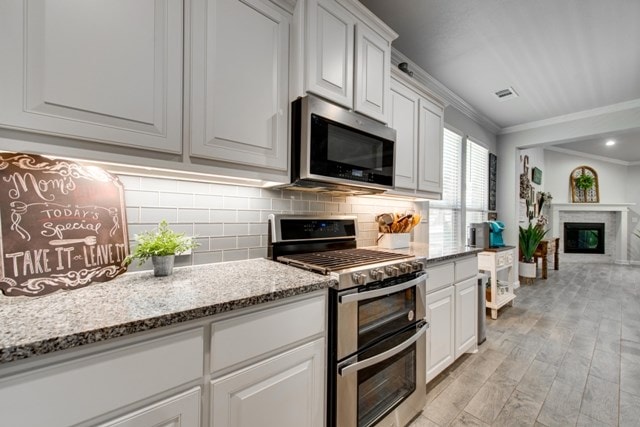 kitchen featuring light stone countertops, ornamental molding, stainless steel appliances, a glass covered fireplace, and tasteful backsplash