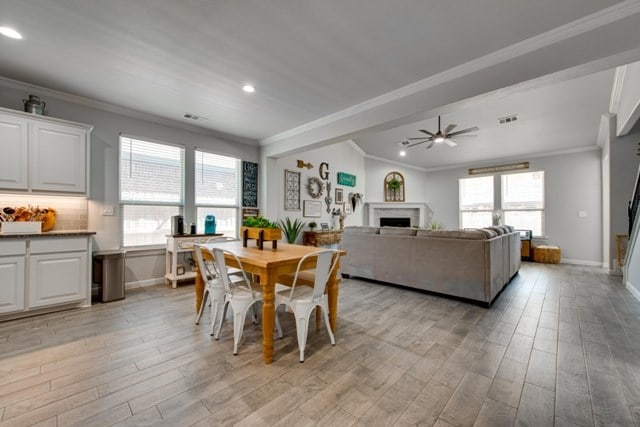 dining space with light wood-style flooring, a fireplace, crown molding, and baseboards