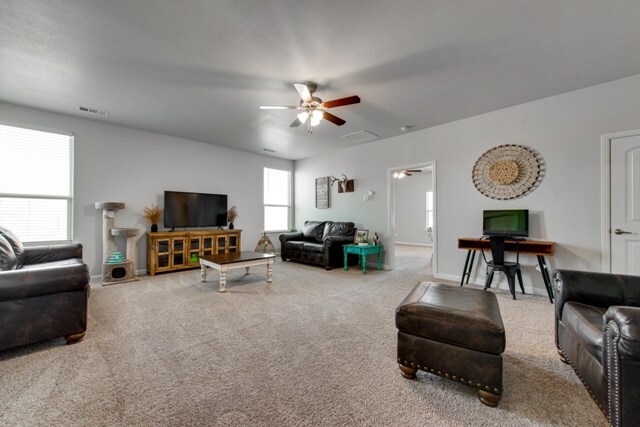 living room with carpet, a ceiling fan, visible vents, and baseboards