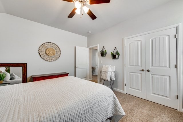 bedroom with a ceiling fan, a closet, baseboards, light colored carpet, and vaulted ceiling