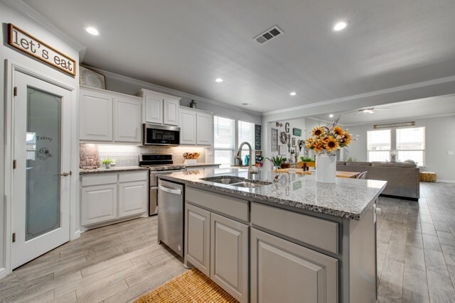 kitchen featuring visible vents, a sink, stainless steel appliances, light wood-style floors, and crown molding