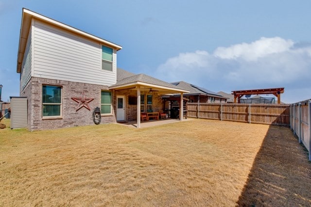 rear view of property featuring a patio, brick siding, a fenced backyard, and a lawn