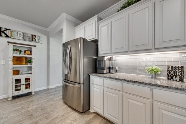 kitchen featuring light wood finished floors, decorative backsplash, white cabinets, crown molding, and stainless steel fridge