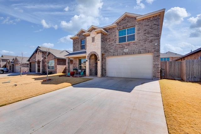 traditional home with a garage, brick siding, a front yard, and fence