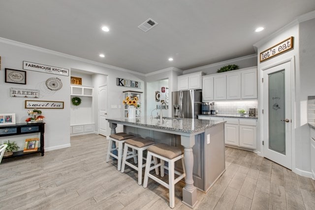 kitchen featuring visible vents, crown molding, a kitchen bar, light wood-style floors, and stainless steel fridge