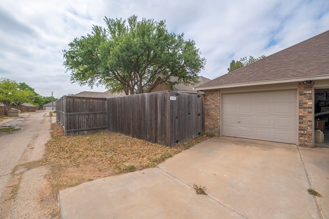 view of home's exterior featuring fence, a shingled roof, concrete driveway, and brick siding