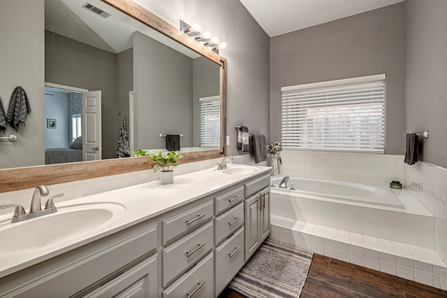 ensuite bathroom with double vanity, a garden tub, visible vents, wood finished floors, and a sink