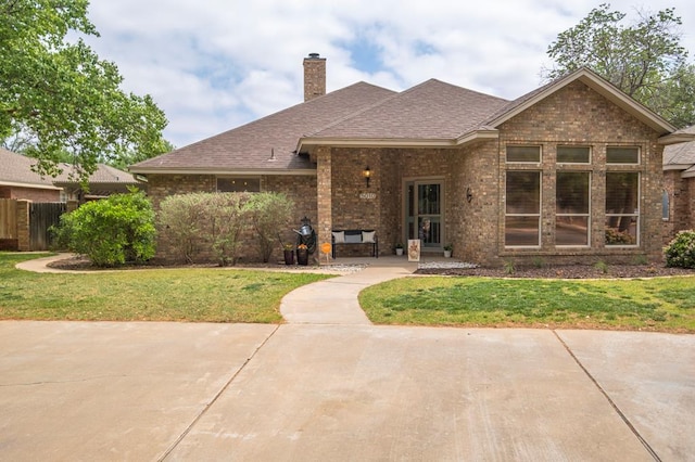 view of front of house featuring roof with shingles, a chimney, a front yard, and brick siding