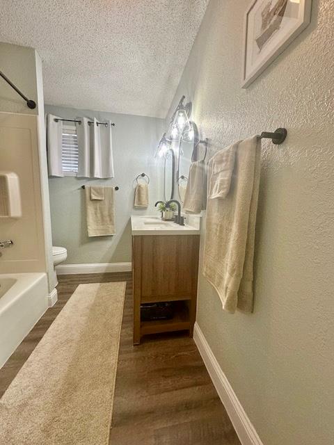 full bathroom featuring hardwood / wood-style flooring, vanity, shower / tub combination, and a textured ceiling