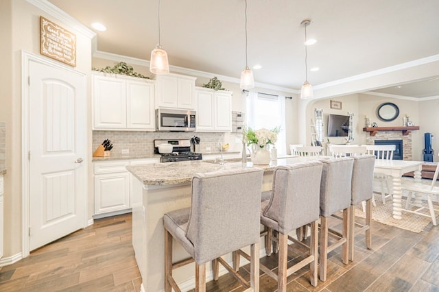 kitchen with white cabinetry, a kitchen island with sink, decorative light fixtures, and appliances with stainless steel finishes