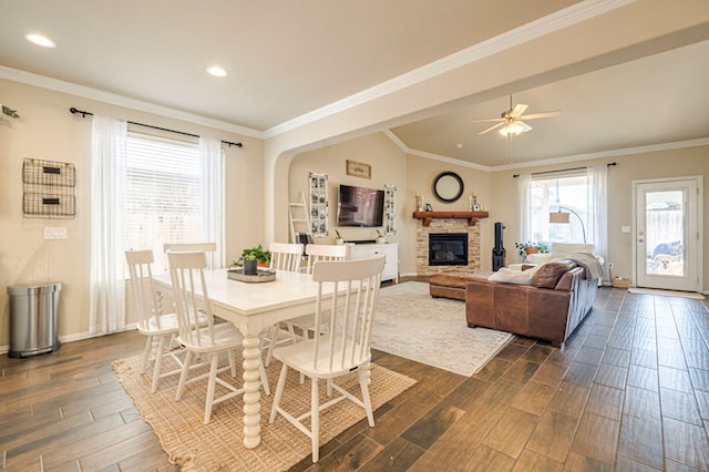 dining area with a stone fireplace, ceiling fan, dark hardwood / wood-style flooring, and ornamental molding