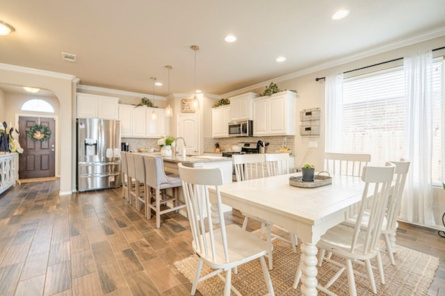 dining area featuring sink, wood-type flooring, and crown molding