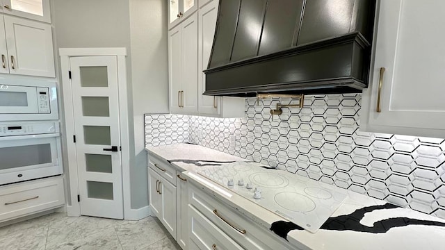 kitchen with white cabinetry, white appliances, light stone countertops, and custom range hood