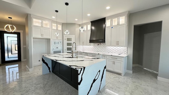 kitchen featuring decorative light fixtures, white cabinetry, custom exhaust hood, a kitchen island with sink, and white appliances