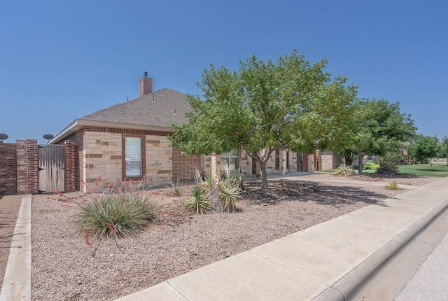 7604 Keyhaven, Odessa, TX 79765 - view of property hidden behind natural elements with stone siding, a gate, a chimney, and a shingled roof