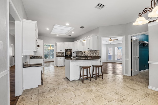 kitchen featuring white cabinetry, tasteful backsplash, hanging light fixtures, oven, and ceiling fan with notable chandelier