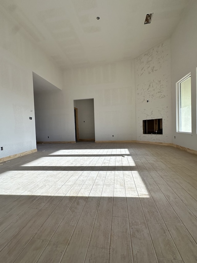unfurnished living room featuring wood finished floors, a high ceiling, a fireplace, and baseboards
