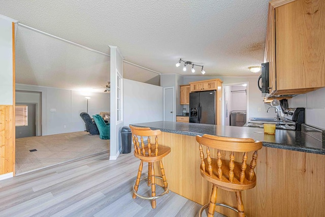 50031 E County Rd 71, Midland, TX 79705 - kitchen with black appliances, light wood-type flooring, a peninsula, dark countertops, and a textured ceiling