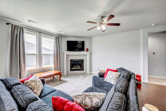 living area featuring light tile patterned floors, a ceiling fan, a glass covered fireplace, visible vents, and baseboards