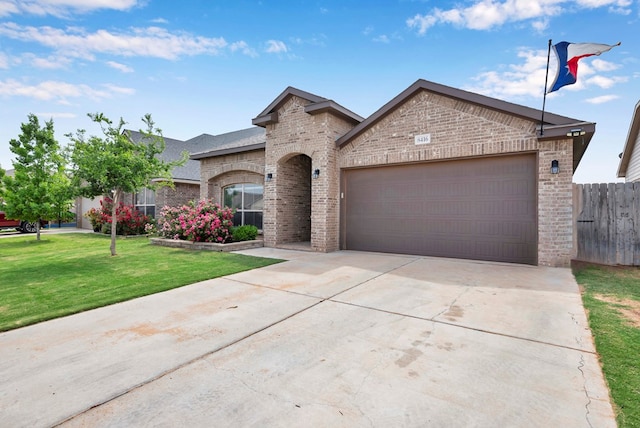 view of front of home with a front yard, fence, brick siding, an attached garage, and concrete driveway