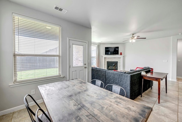 dining space featuring a glass covered fireplace, baseboards, light tile patterned floors, visible vents, and ceiling fan