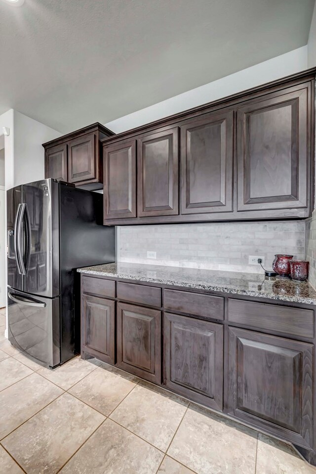 kitchen with decorative backsplash, light stone counters, stainless steel refrigerator with ice dispenser, and dark brown cabinetry