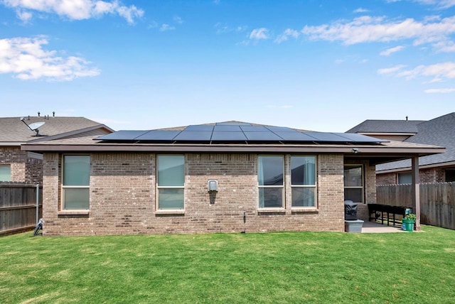 back of property featuring a patio area, brick siding, a fenced backyard, a lawn, and roof mounted solar panels