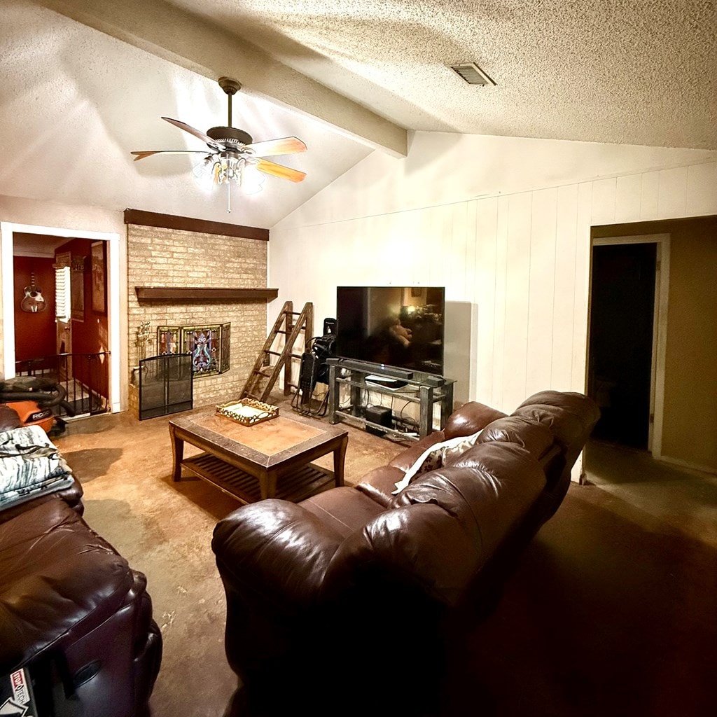 carpeted living room featuring a ceiling fan, a textured ceiling, and a brick fireplace